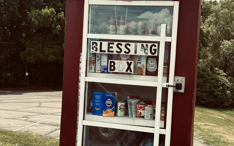A dark red Blessing Box with its door open and shelves stocked with canned goods