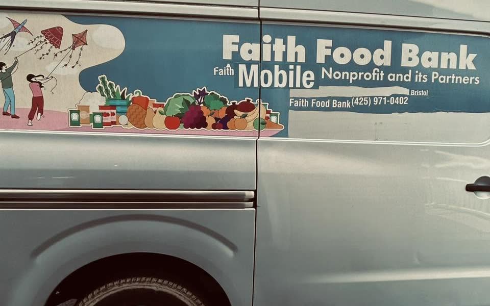 The Faith Mobile Food Bank van, a light blue cargo van with the food bank's name, artwork and phone number on the side